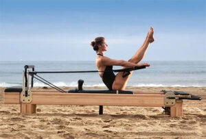 Ragazza che esegue esercizi di pilates reformer su una spiaggia con mare sullo sfondo