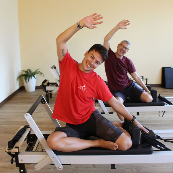 Coppia di uomini che eseguono esercizi su postazione pilates reformer